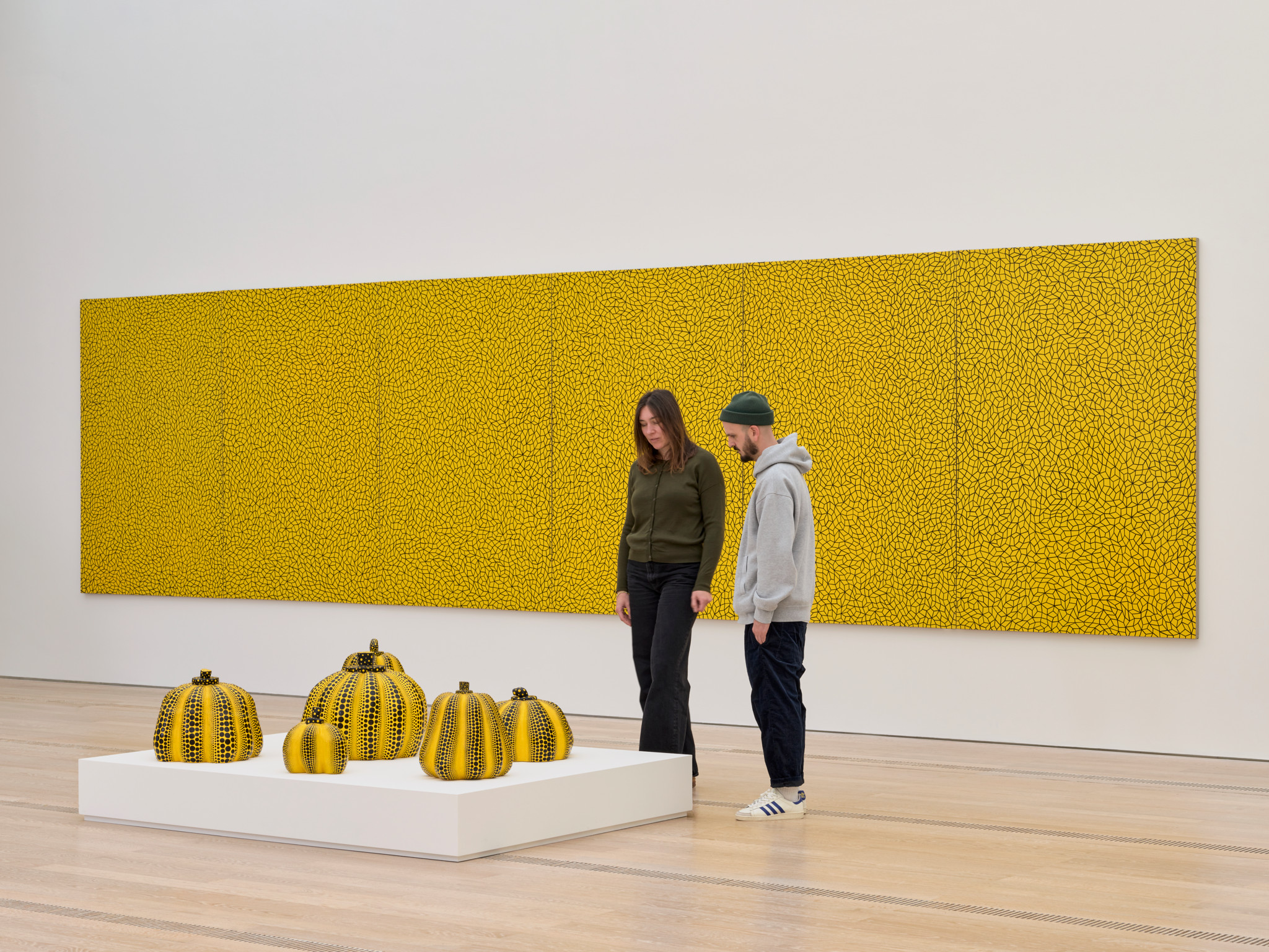 Zwei Personen betrachten gelbe Kürbis-Skulpturen von Yayoi Kusama in der Fondation Beyeler, im Hintergrund ist ein grosses Gemälde der Japanerin zu sehen.