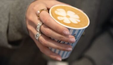 Elegante Frauenhand hält Kaffeebecher mit Kleeblatt aus Milchschaum