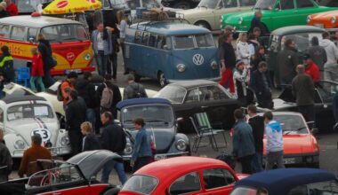 Menschen besichtigen auf einem Parkplatz viele alte VW-Käfer und andere Fahrzeugen