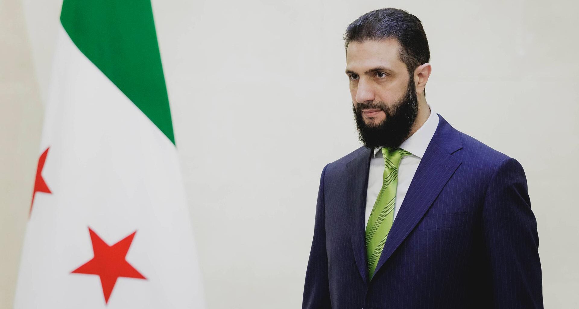 Ahmad Al-Scharaa steht neben der Flagge Syriens