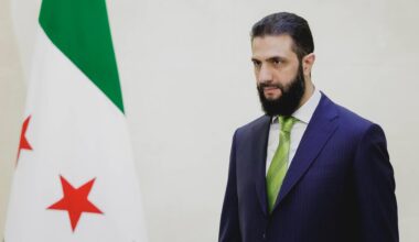 Ahmad Al-Scharaa steht neben der Flagge Syriens
