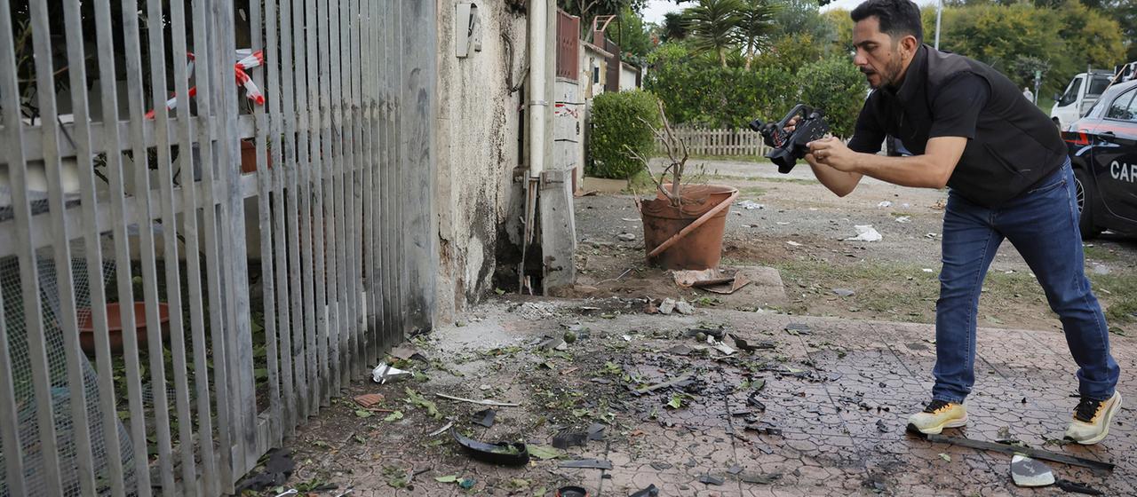 Ein Reporter filmt Teile eines Autos, die auf dem Boden liegen, nachdem unter dem Auto in Pome ein Sprengsatz detoniert ist. | AP Ein Reporter filmt Teile eines Autos, die auf dem Boden liegen, nachdem unter dem Auto in Pome ein Sprengsatz detoniert ist.