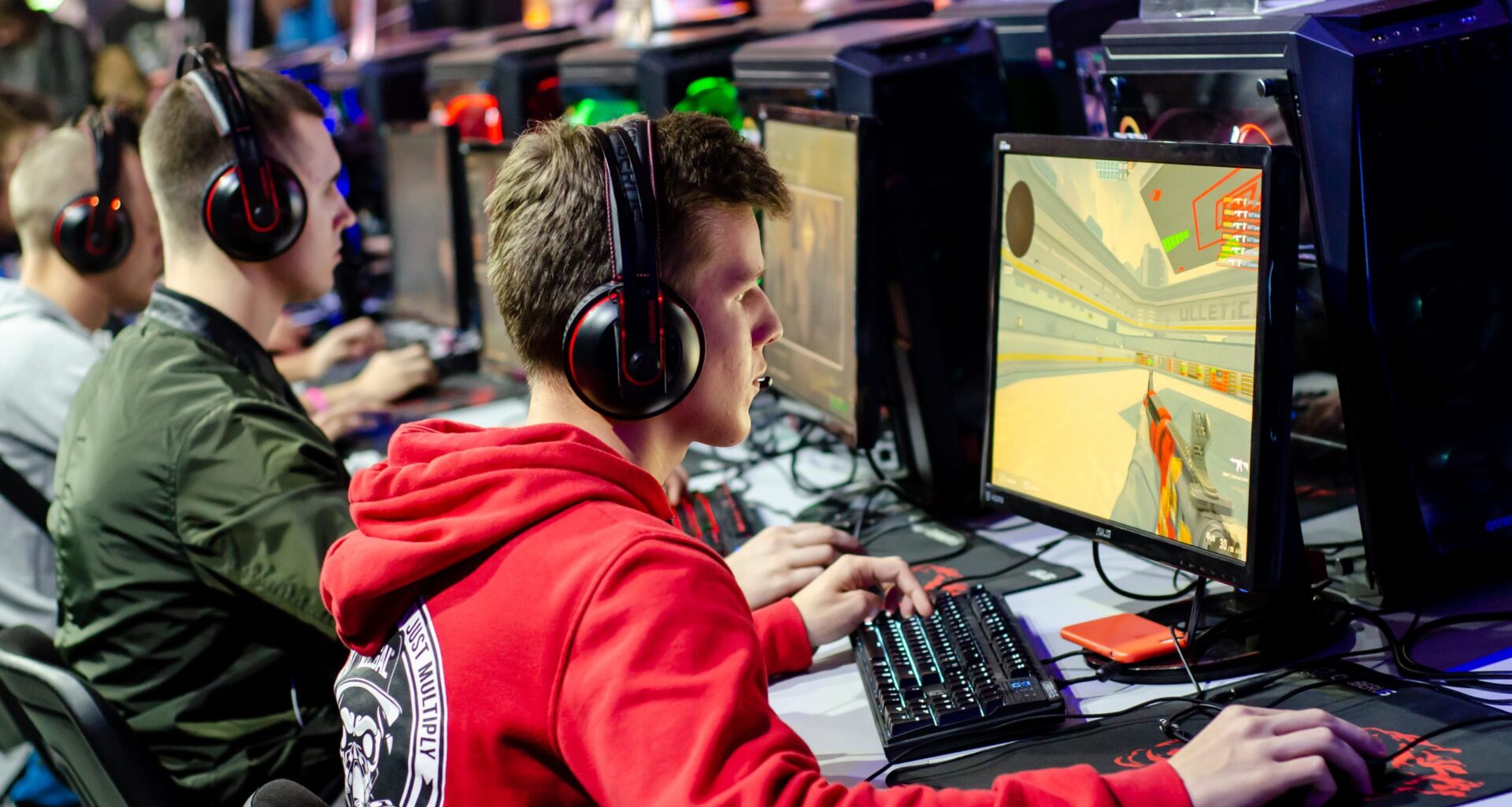 Mehrere junge Leute mit Headsets sitzen an Computern und spielen CS2, ein Ego-Shooter-Videospiel, bei einem esports-Event oder Gaming-Turnier.