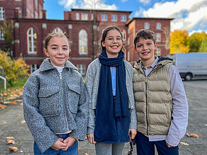 Charlotte (10), Ingelotte (12) und Ferdinand (10) stehen nebeneinander vor dem Schulgebäude.