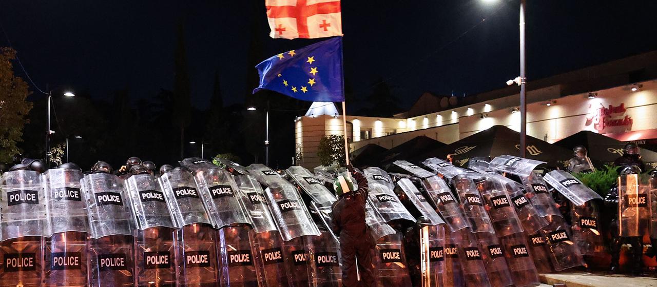 Ein Demonstrant schwenkt in der Innenstadt von Tiflis vor der Bereitschaftspolizei eine georgische und eine EU-Flagge. (Archivbild: 4.10.2025) | AFP Ein Demonstrant schwenkt in der Innenstadt von Tiflis vor der Bereitschaftspolizei eine georgische und eine EU-Flagge. (Archivbild: 4.10.2025)