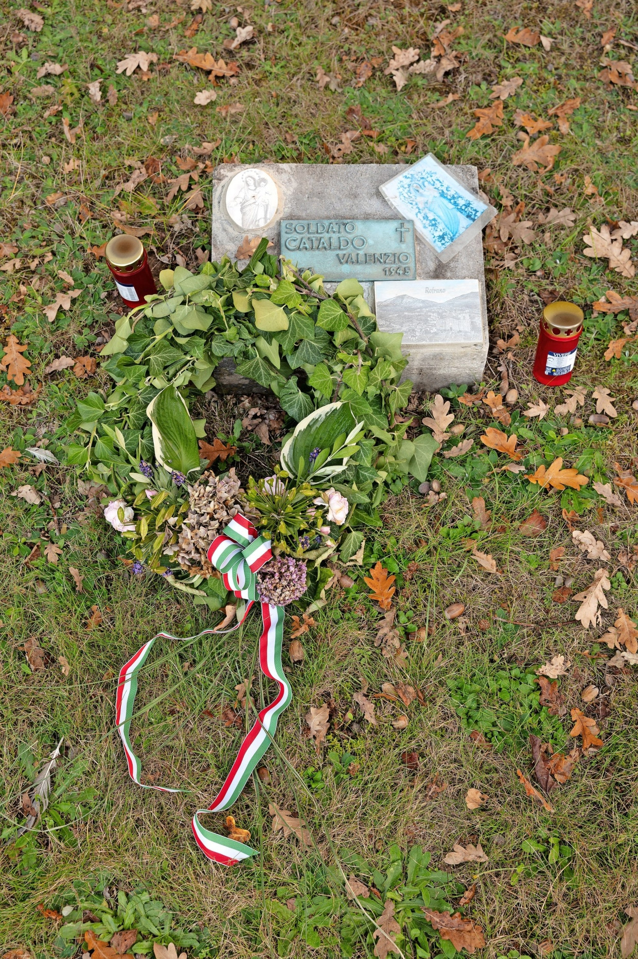Ein Kranz und Kerzen am Grab eines 1945 gefallenen italienischen Soldaten auf dem Cimitero di Guerra Italiano.