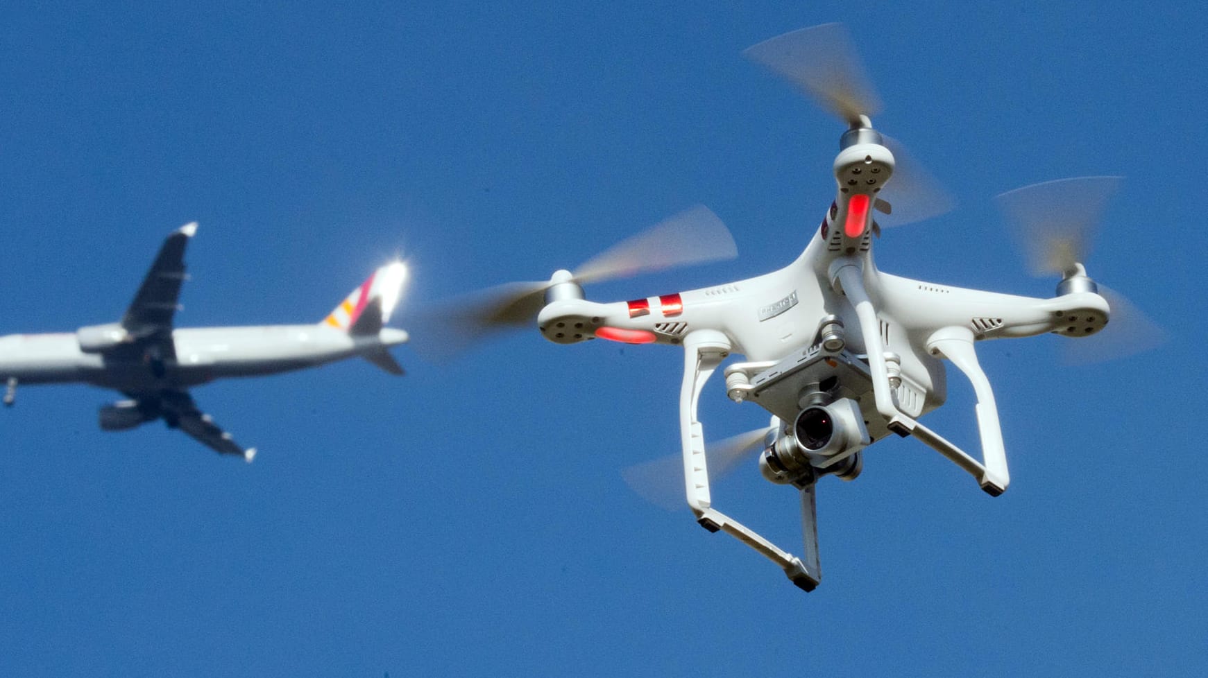 Eine private Drohne fliegt in knapp 10 Metern Flughöhe, als in weiter Entfernung ein Flugzeug beim Anflug auf einen Flughafen zu sehen ist (Symbolbild): Wegen einer Drohnensichtung ist der Betrieb am Frankfurter Flughafen schon am Donnerstag eingestellt worden.