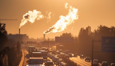 Stau am Morgen auf der Autobahn, im Gegenlicht sind im Hintergrund Rauschschwaden aus Industrieschornsteinen zu erkennen.