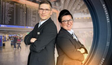 Dimitar Marinov und Nese Altay-Breuer stehen Rücken an Rücken im Terminal des Frankfurter Flughafens. Beide schauen lächelnd in die Kamera. Im Hintergrund laufen Personen unter der Abflugtafel.