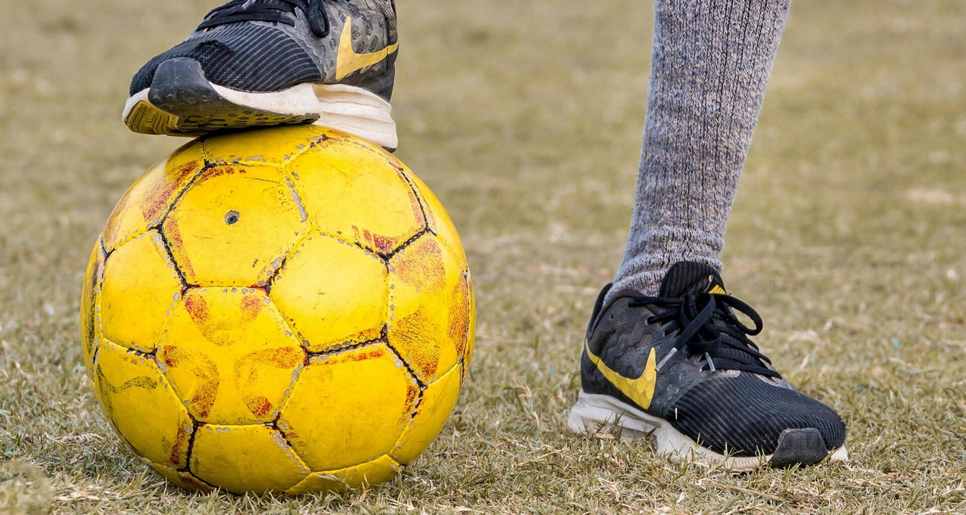 Ein Fußballer hat einen Fuß auf einen gelben Ball stellt.