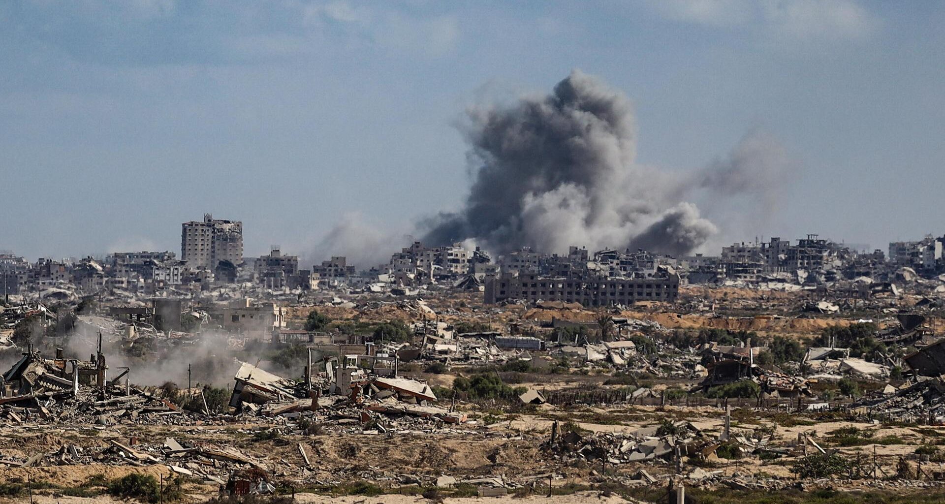 Block aus großer Ferne auf eine besiedelte Gegend im Gazastreifen. Am Horizont steigt Rauch auf.