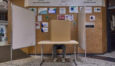 Blick auf eine Wahlkabine in einer Schule in Hamburg. Ein Mann sitzt an einem Tisch. Er wird von einem Sichtschutz verdeckt.
