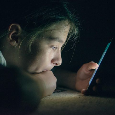 Ein Teenager starrt in einem abgedunkelten Raum auf ein Handy-Display Ein Teenager starrt in einem abgedunkelten Raum auf ein Handy-Display