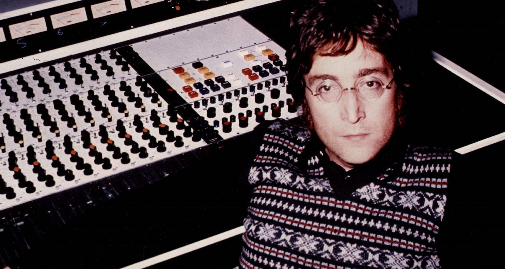 John Lennon sitzt an einer Studiokonsole aus den Siebzigern und blickt ernst in die Kamera
