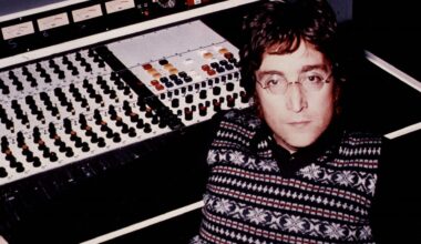 John Lennon sitzt an einer Studiokonsole aus den Siebzigern und blickt ernst in die Kamera