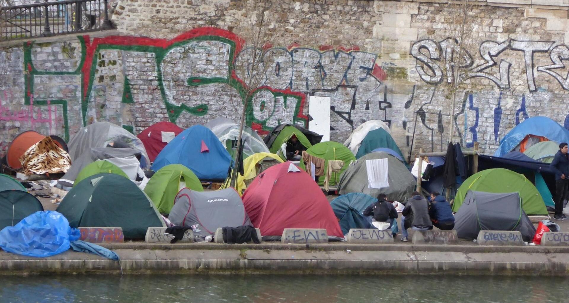 Blick vom anderen Seine-Ufer auf zahlreiche bunte Zelte an einer Ufermauer am Kai.