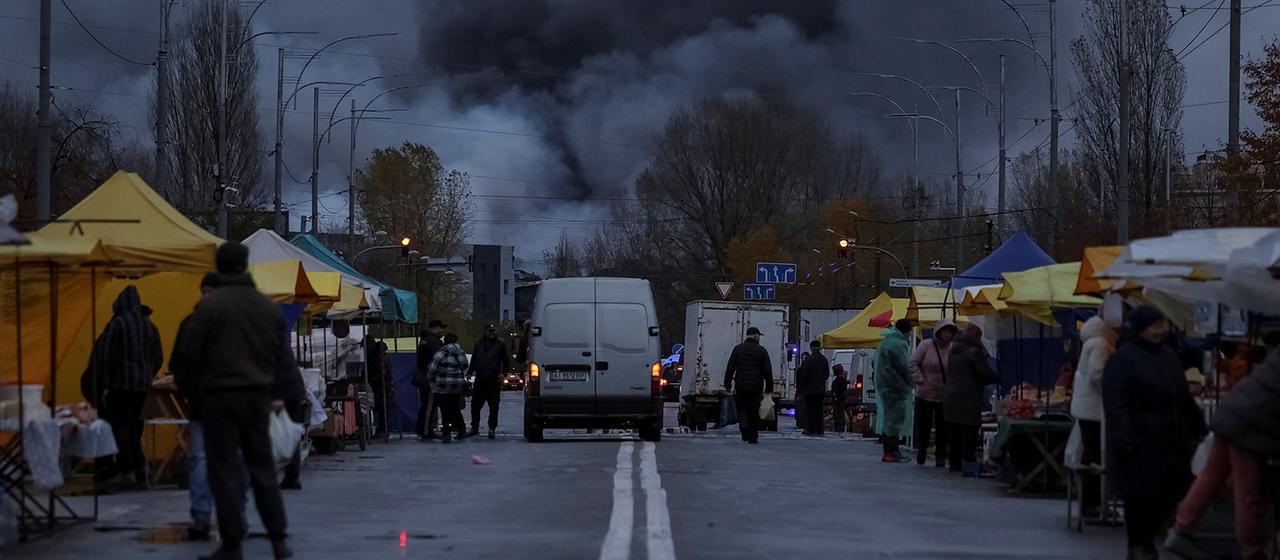 Menschen stehen auf einer Straße mit Marktständen, im Hintergrund steigt dichter schwarzer Rauch in den Himmel. | REUTERS Menschen stehen auf einer Straße mit Marktständen, im Hintergrund steigt dichter schwarzer Rauch in den Himmel.