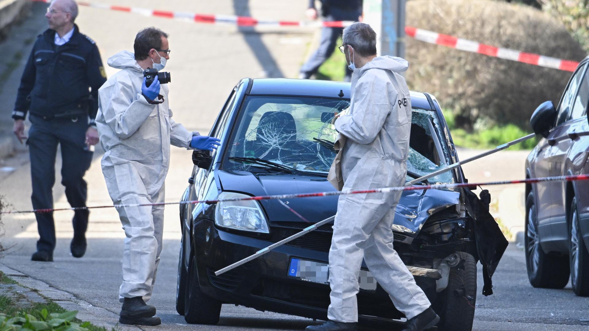 Polizisten in Einweganzügen laufen um einen verbeulten Kleinwagen herum.