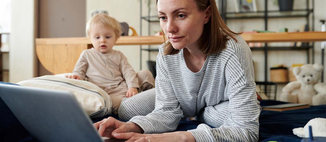 Frau mit Kleinkind sitzt vor einem Laptop. | picture alliance / AnnaStills Frau mit Kleinkind sitzt vor einem Laptop.