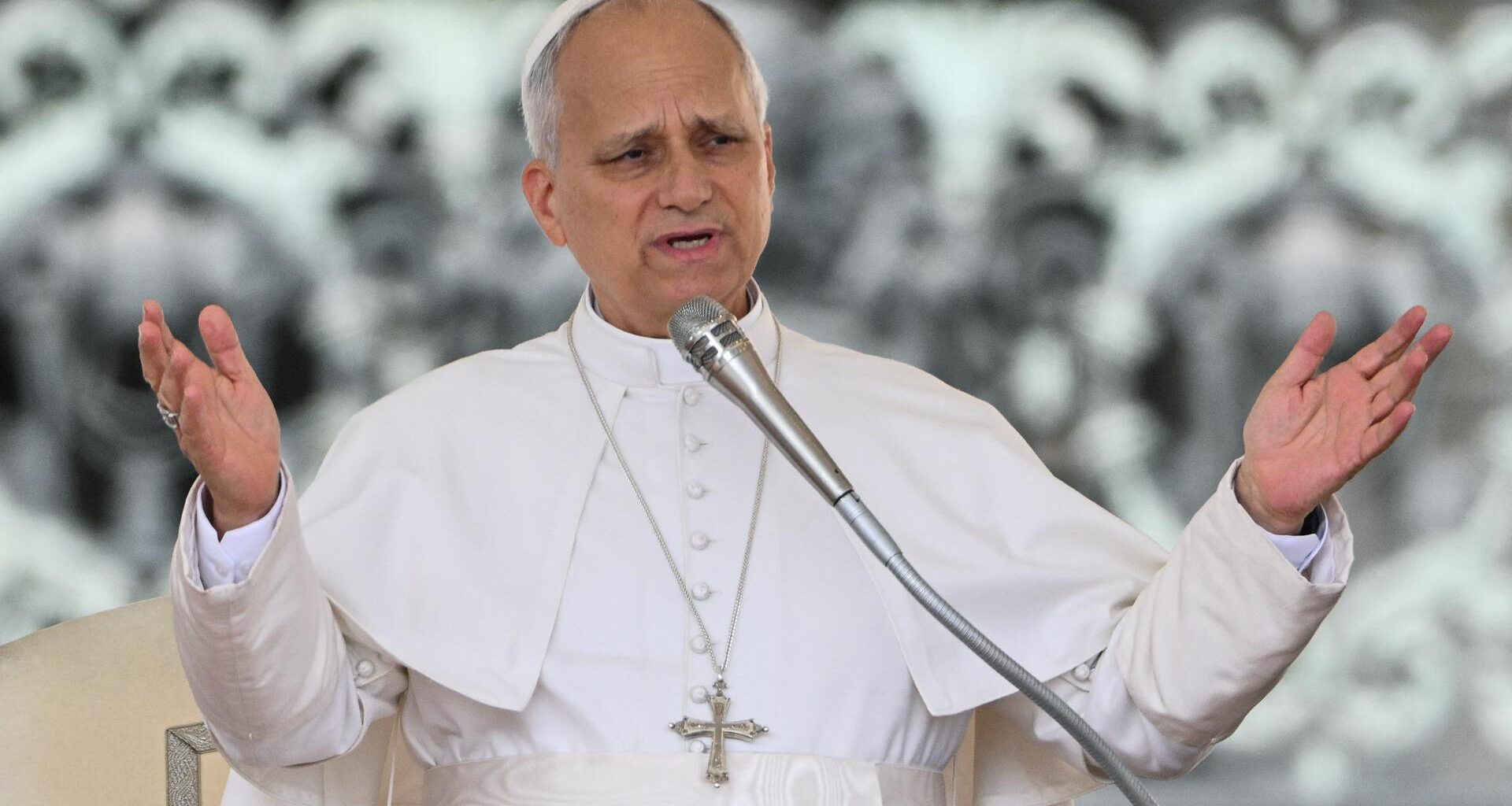 Papst Leo hat seine Arme ausgebreitet und spricht in ein Mikrofon.