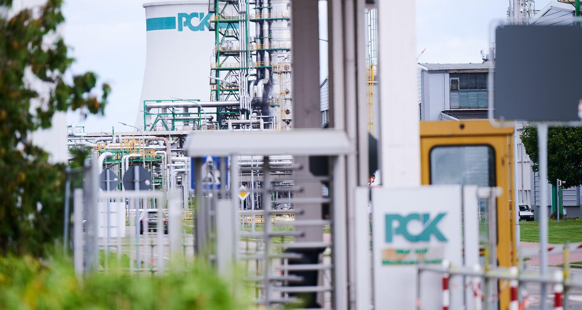Das Bild zeigt das Werksgelände der Raffinerie PCK in Schwedt. Das Logo PCK ist im Vordergrund am Eingang zu sehen und im Hintergrund an einem Tank.