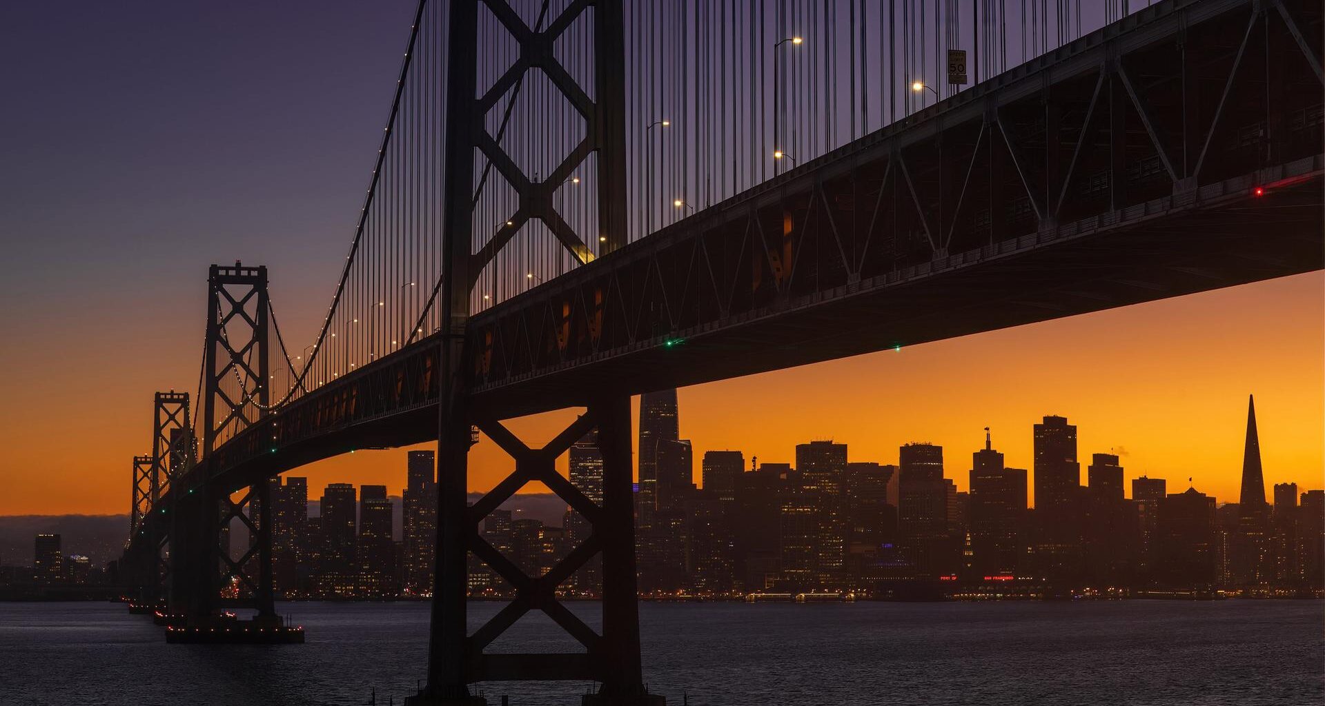 Die Bay Bridge am frühen Abend in San Francisco. Im Hintergrund geht die Sonne unter.