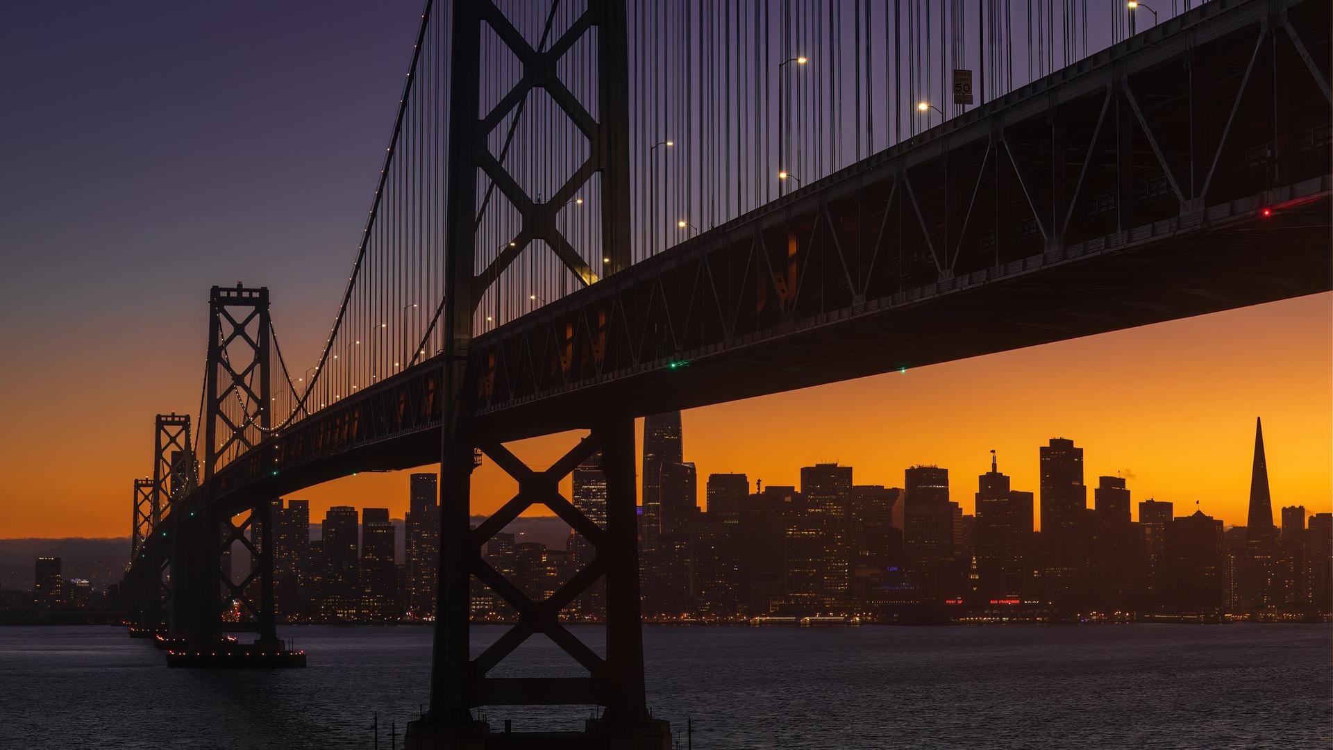 Die Bay Bridge am frühen Abend in San Francisco. Im Hintergrund geht die Sonne unter. 