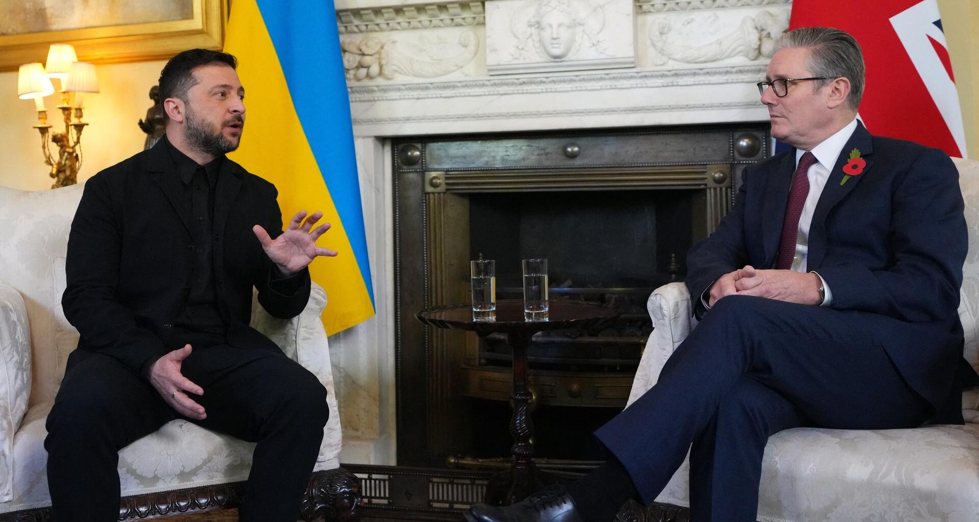 Der ukrainische Präsident Wolodymyr Selensykj (l.) und der britische Premierminister Keir Starmer (r.) sitzen nebeneinander, hinter ihnen die Nationalflaggen. Selenskyj spricht und gestikuliert.