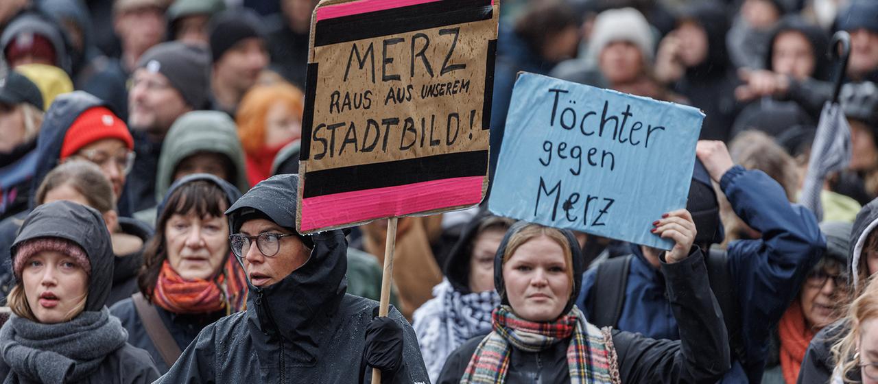 Teilnehmende halten auf einer Demonstration in Hamburg Schilder mit den Aufschriften "Merz raus aus dem Stadtbild!" und "Töchter gegen Merz".  | dpa Teilnehmende halten auf einer Demonstration in Hamburg Schilder mit den Aufschriften "Merz raus aus dem Stadtbild!" und "Töchter gegen Merz".