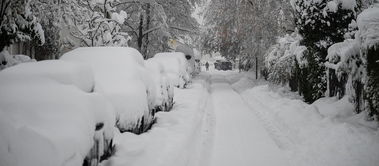 Hohe Schneemassen liegen auf Autos und einer Straße. | picture alliance/dpa Hohe Schneemassen liegen auf Autos und einer Straße.