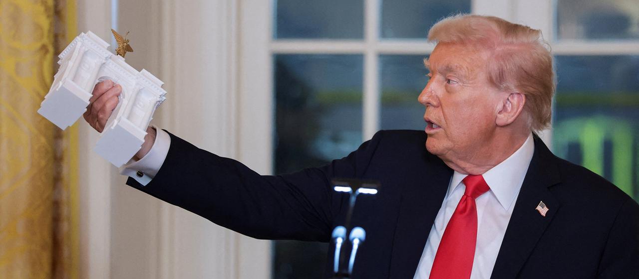 Donald Trump hält ein Modell eines monumentalen Bogens.