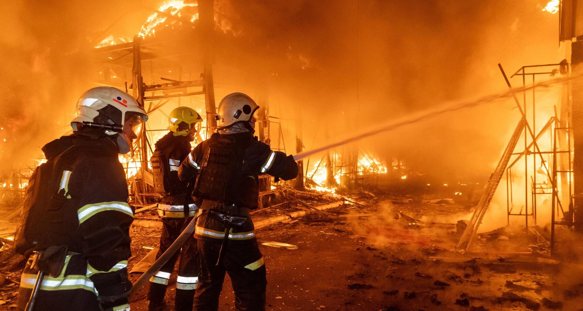 Drei Feuerwehrleute verspritzen mit einem Schlauch Wasser in die lichterloh brennende Marktruine.