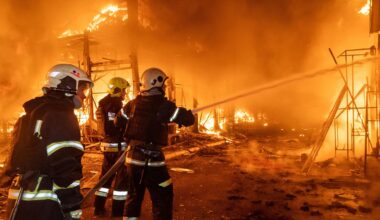 Drei Feuerwehrleute verspritzen mit einem Schlauch Wasser in die lichterloh brennende Marktruine.