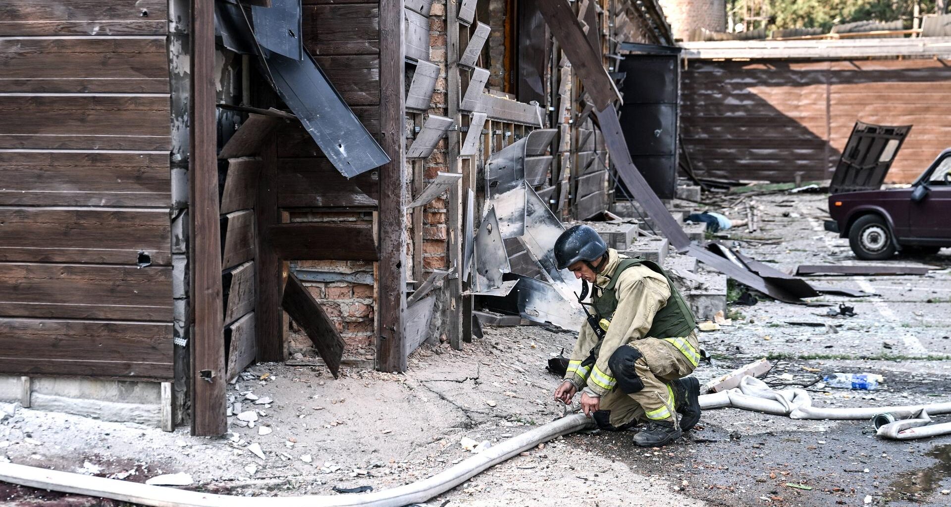 Ein Feuerwehrmann kniet mit einem Wasserschlauch vor einer zerstörten Hütte.