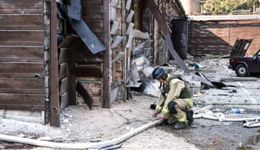 Ein Feuerwehrmann kniet mit einem Wasserschlauch vor einer zerstörten Hütte.