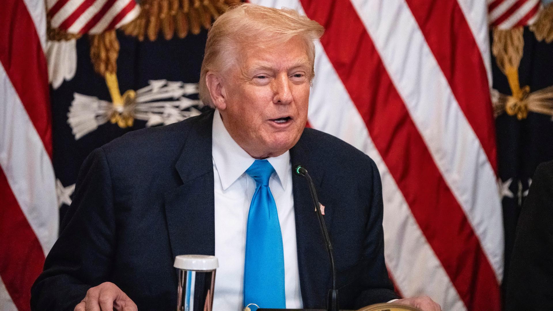 US-Präsident Donald Trump spricht im Weißen Haus zum Thema "Making Health Technology Great Again". Er sitzt an einem Schreibtisch, hinter ihm die Flagge der Vereinigten Staaten von Amerika.