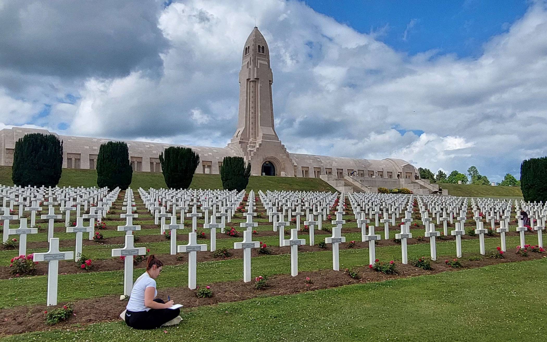  Eine Schülerin aus Rheinbach arbeitet im Juni 2025 vor den Gräbern der Gedenkstätte in Verdun – im Hintergrund das Beinhaus – an einer Aufgabe. 