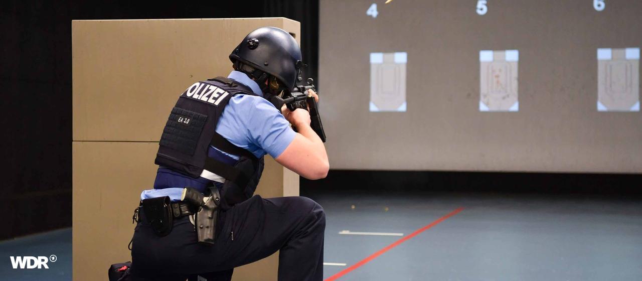 Eine Person mit Helm und Weste der Polizei, kniet vor zwei Karton und zielt mit einer Waffe auf Ziele