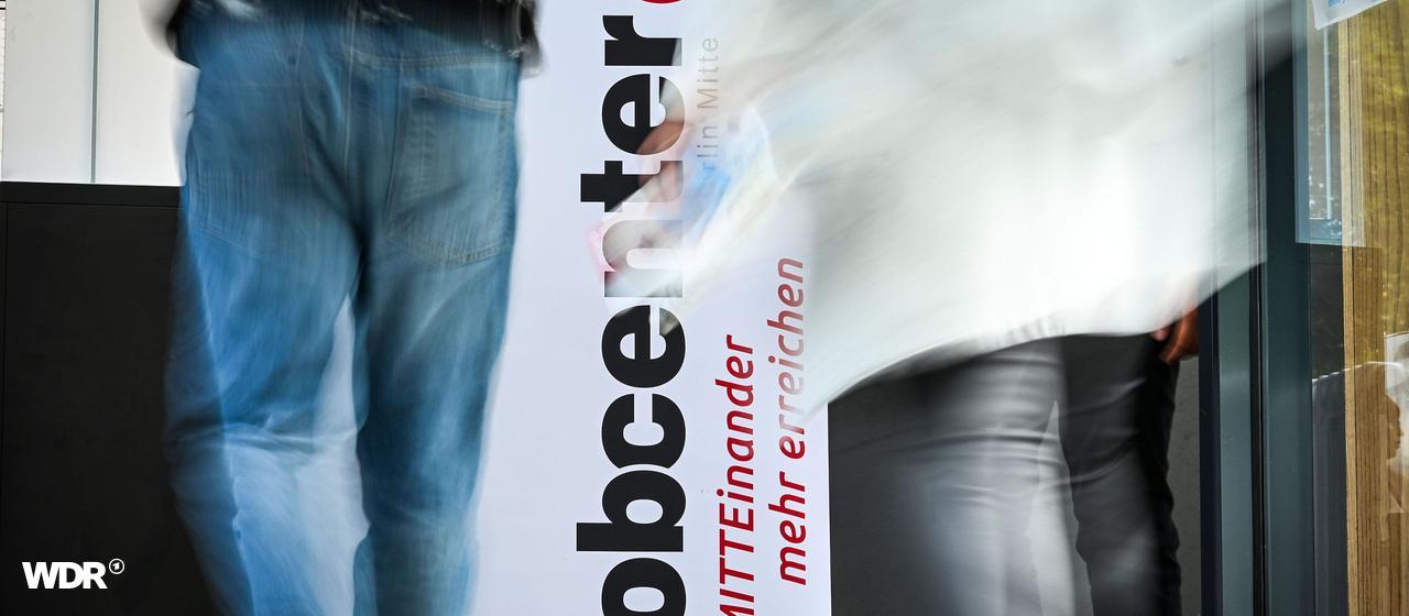 Sozialmissbrauch: Fachkongress soll Behörden besser vernetzen | Jens Kalaene / dpa Personen gehen am Logo vom Jobcenter vorbei.