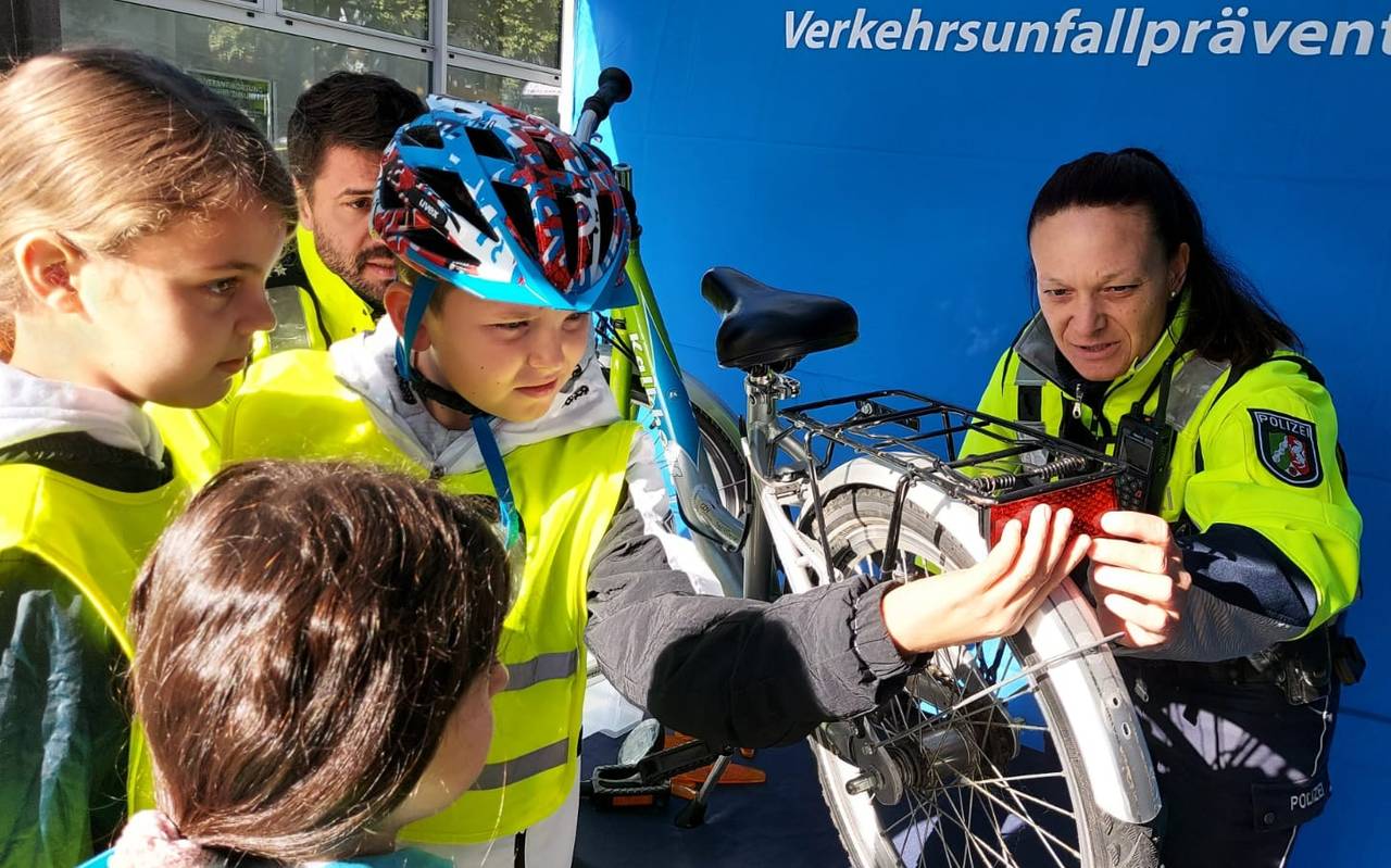 Ein Junge mit gelber Warnweste hält eine Rücklampe an ein Fahrrad. Daneben steht eine Polizistin.