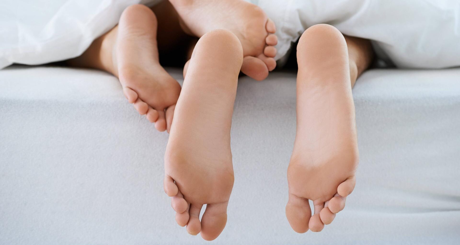 Unter einer Bettdecke schauen zwei Paar Füße hervor.