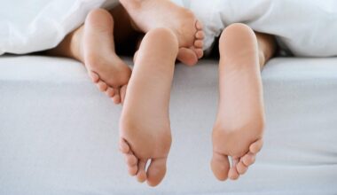 Unter einer Bettdecke schauen zwei Paar Füße hervor.