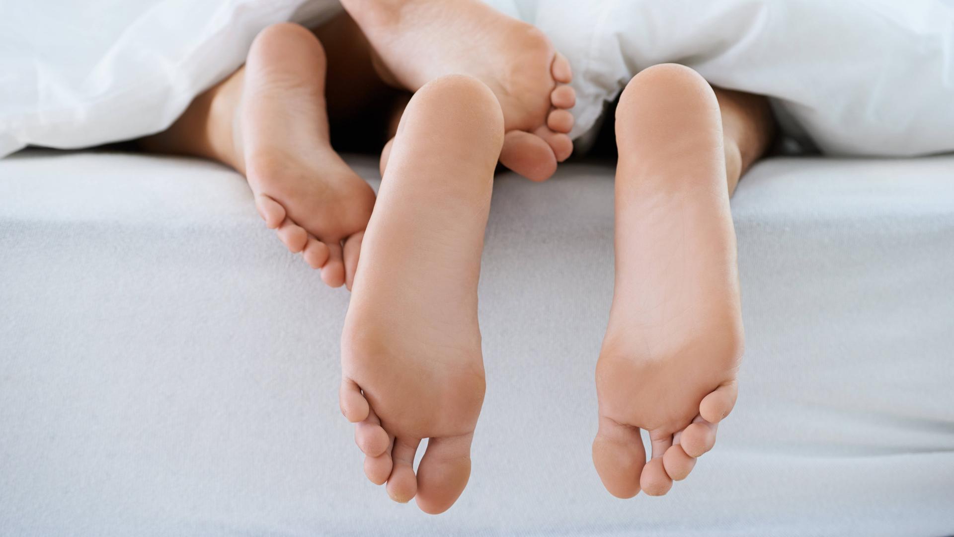 Unter einer Bettdecke schauen zwei Paar Füße hervor.