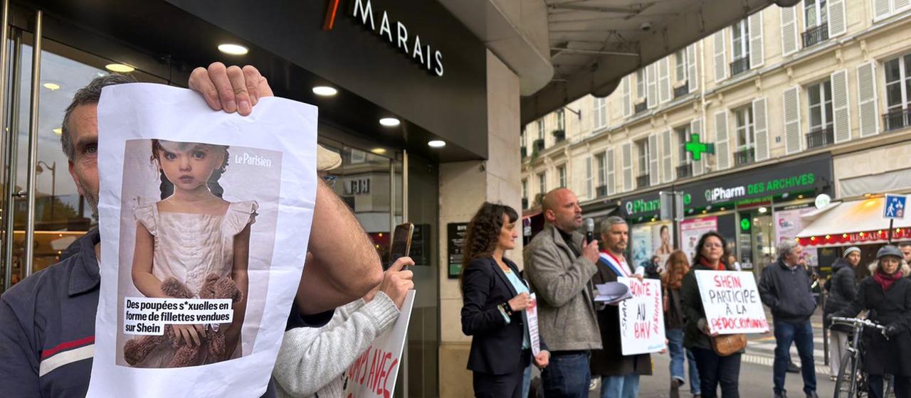 Ein Demonstrant hält ein Bild einer kindlichen Sexpuppe vor dem Kaufhaus BHV Marais in Paris. | AP Ein Demonstrant hält ein Bild einer kindlichen Sexpuppe vor dem Kaufhaus BHV Marais in Paris.