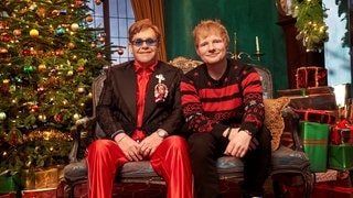 Elton John und Ed Sheeran sitzen auf einem Sofa in einem weihnachtlich geschmüchten Raum. Zusammen singen sie den Christmas-Hit „Merry Christmas“. (Foto: Asylum_Atlantic_Zakary Walters) Elton John und Ed Sheeran sitzen auf einem Sofa in einem weihnachtlich geschmüchten Raum. Zusammen singen sie den Christmas-Hit „Merry Christmas“.