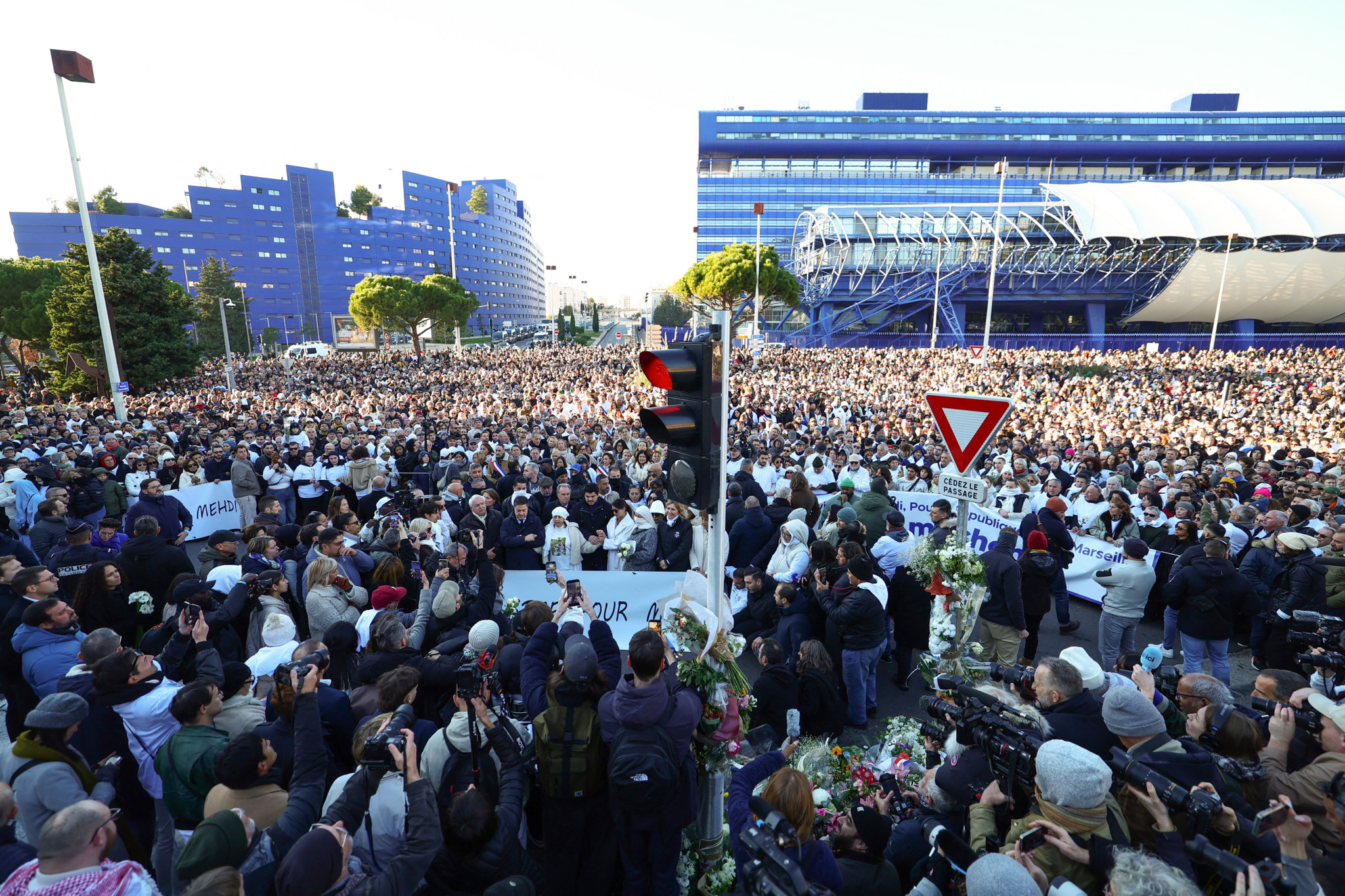 Eine grosse Menschenmenge versammelt sich an einem Kreisverkehr in Marseille zur Gedenkfeier und Protestmarsch gegen Drogenhandel, initiiert von Amine Kessaci und anderen, um Mehdi Kessaci zu ehren, der an diesem Ort ermordet wurde. Im Hintergrund sind moderne Gebäude und Transparente mit Botschaften zu sehen. Eine grosse Menschenmenge versammelt sich an einem Kreisverkehr in Marseille zur Gedenkfeier und Protestmarsch gegen Drogenhandel, initiiert von Amine Kessaci und anderen, um Mehdi Kessaci zu ehren, der an diesem Ort ermordet wurde. Im Hintergrund sind moderne Gebäude und Transparente mit Botschaften zu sehen.
