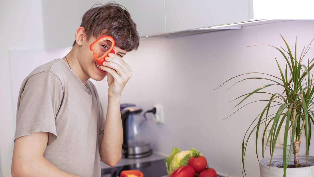 Fröhlicher zufriedener Jugendlicher, der in der Küche einen Gemüsesalat zubereitet 
