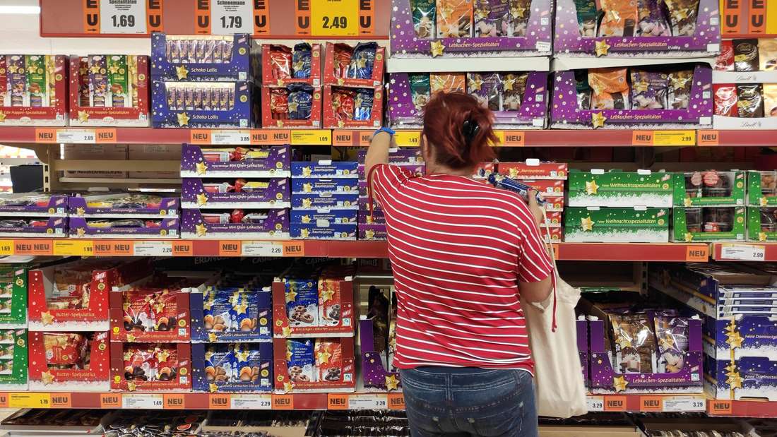 Eine Supermarkt-Kundin steht vor einem Regal mit Weihnachtsleckereien. 