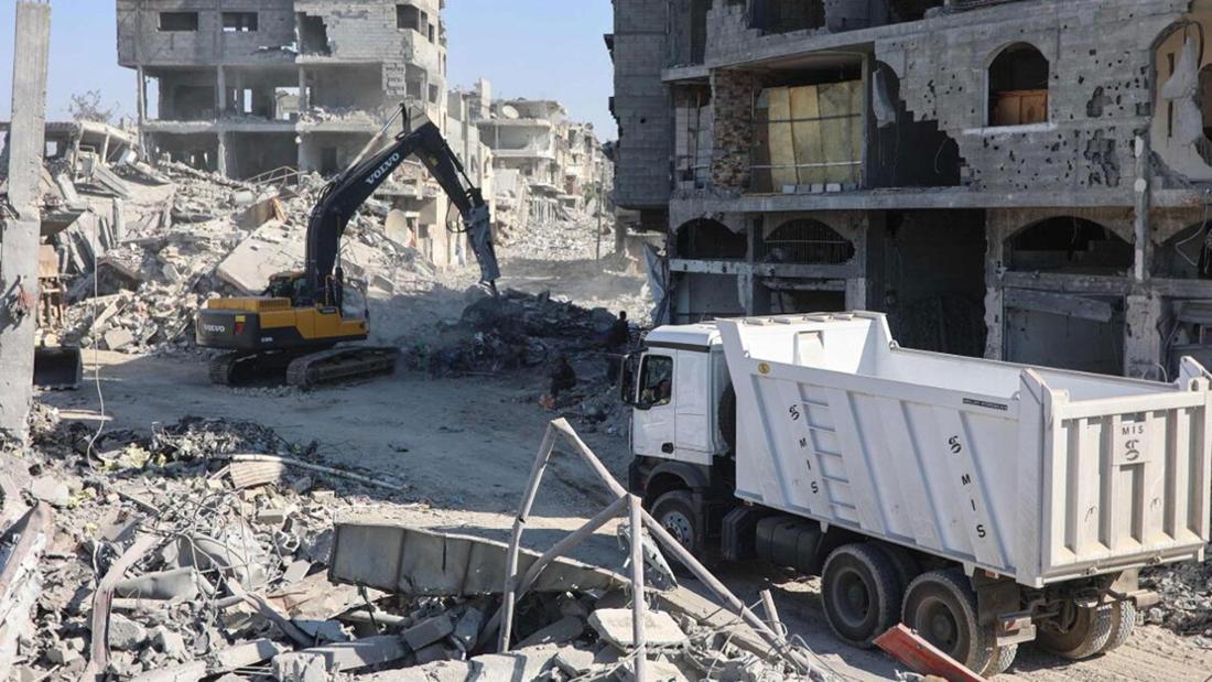 Bagger und Lastwagen stehen in zerstörter Stadt