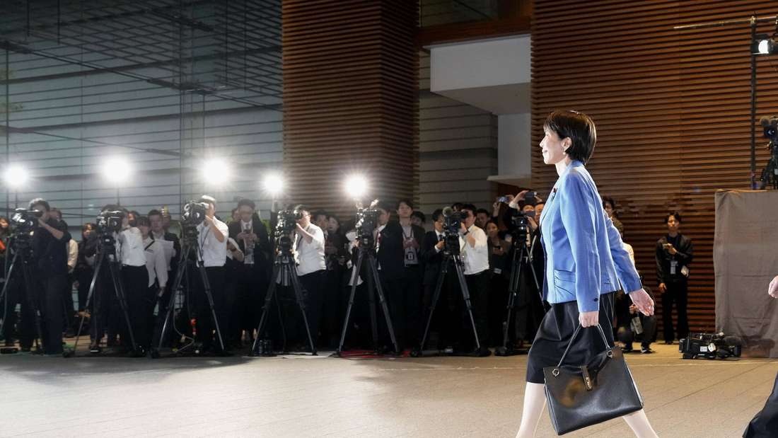 Japans neue Premierministerin Sanae Takaichi schreitet mit Handtasche vor Fotografen und Kameras.